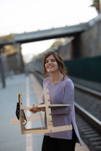 A woman standing on the side of train tracks holding a guitar.