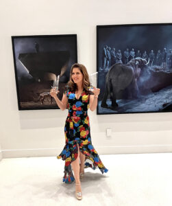 A woman in a colorful dress standing next to two paintings.